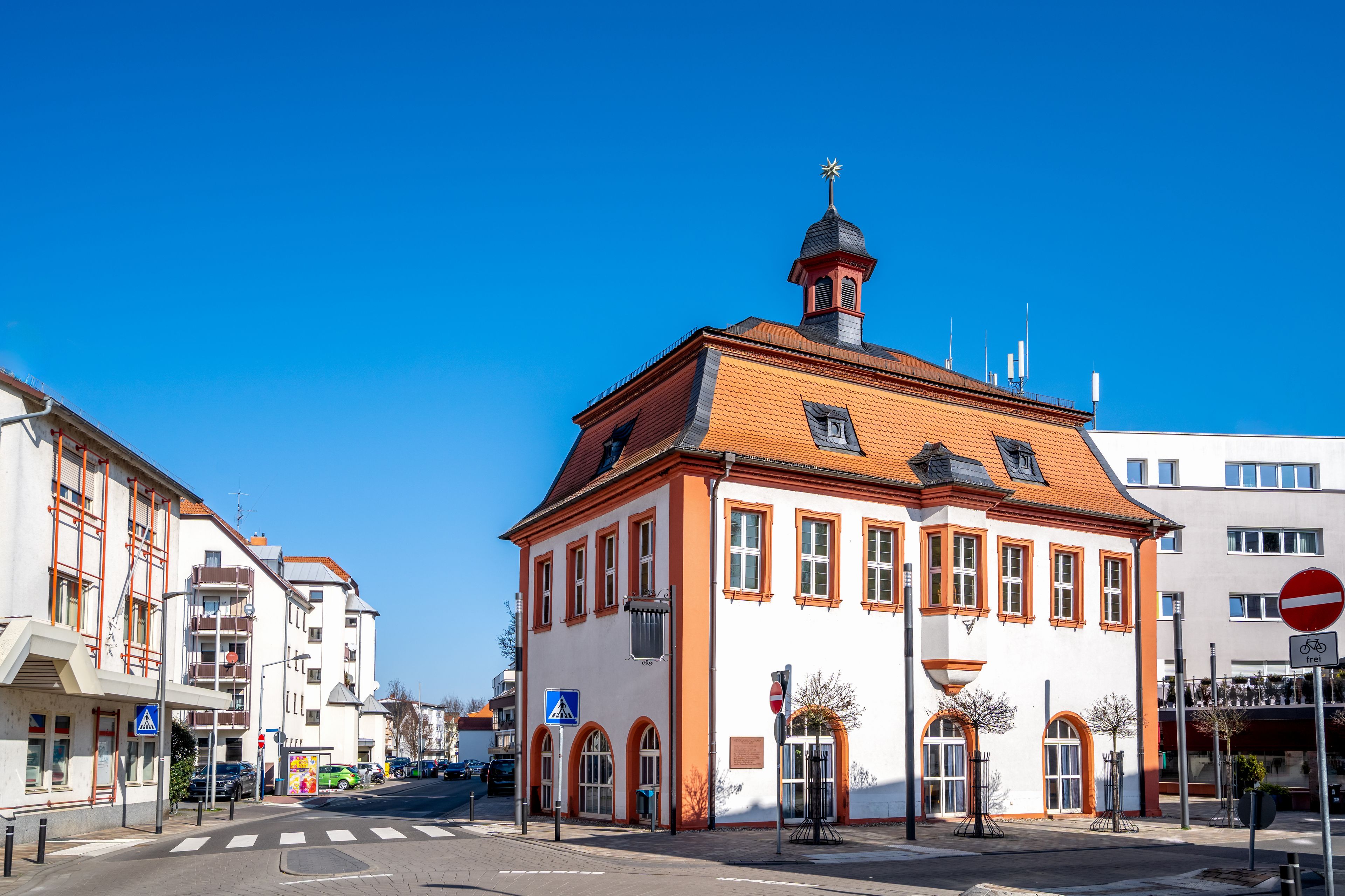 Um edifício histórico com telhado de telhas vermelhas e uma torre, rodeado por edifícios modernos.