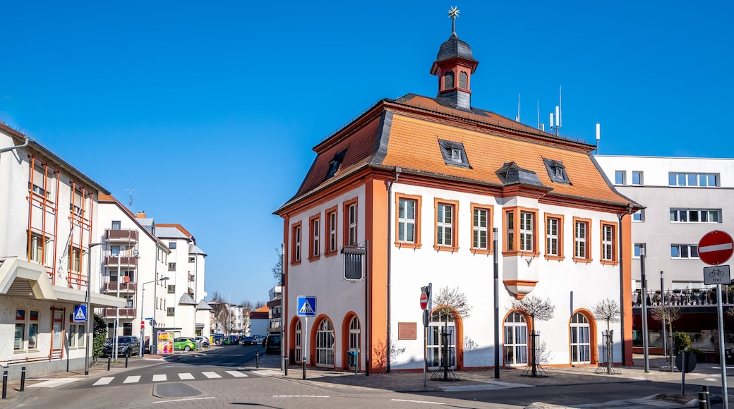 Um edifício histórico com telhado de telhas vermelhas e uma torre, rodeado por edifícios modernos.
