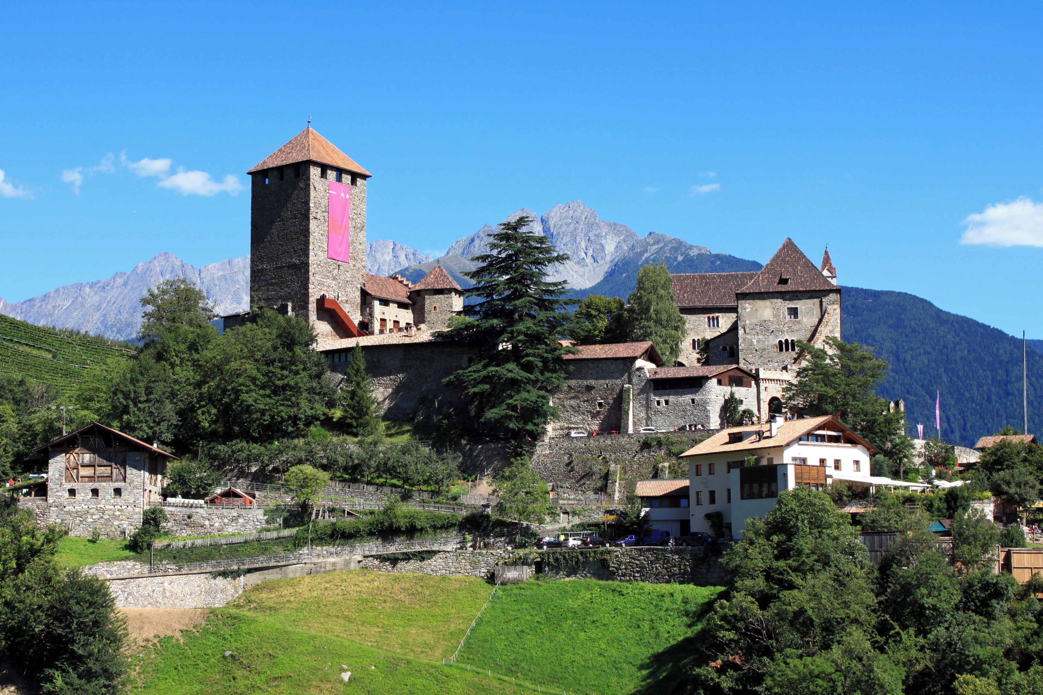 A historic village with stone buildings, a prominent tower, and mountains in the background.