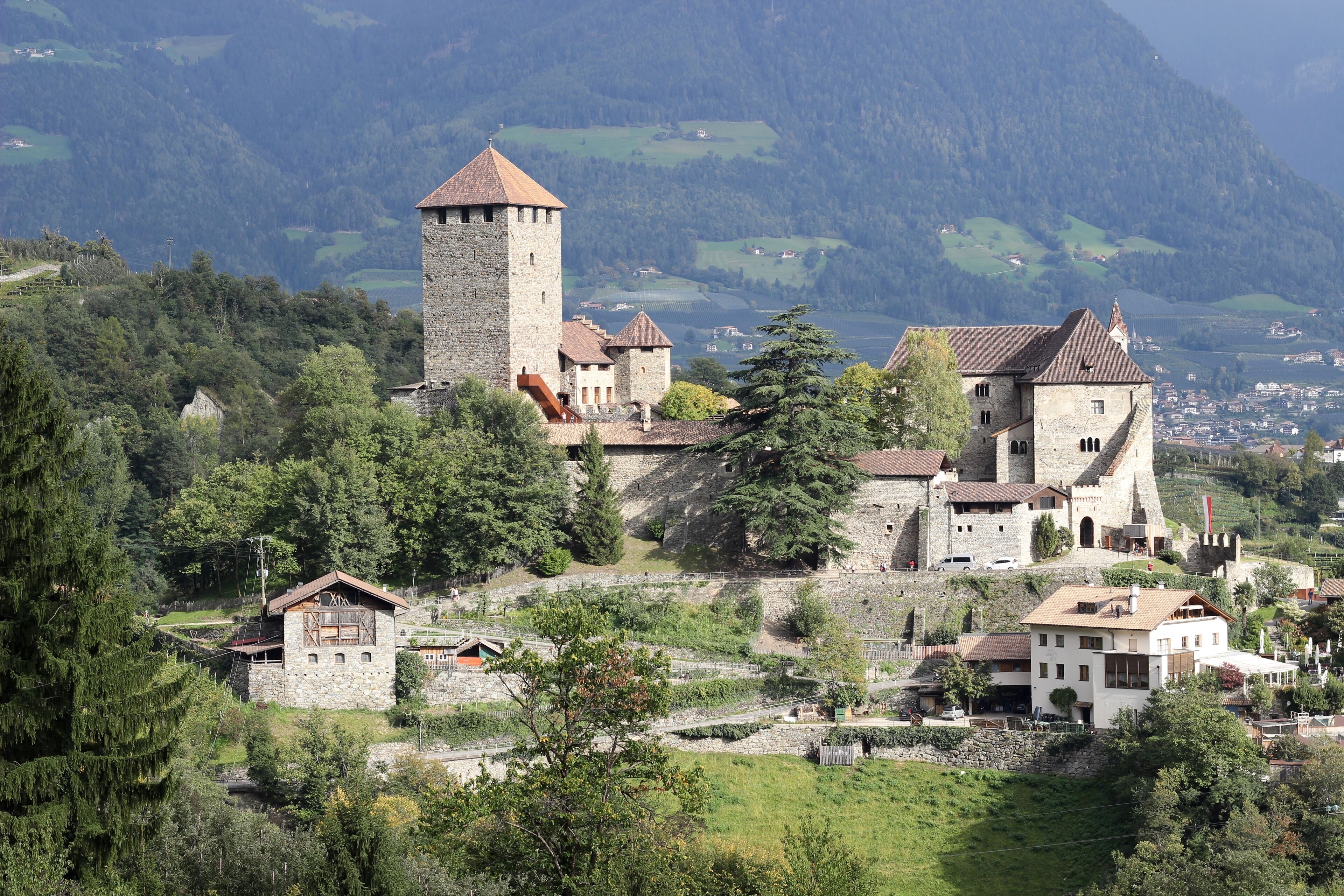 A historic town with a prominent tower, surrounded by lush greenery and mountains in the background.