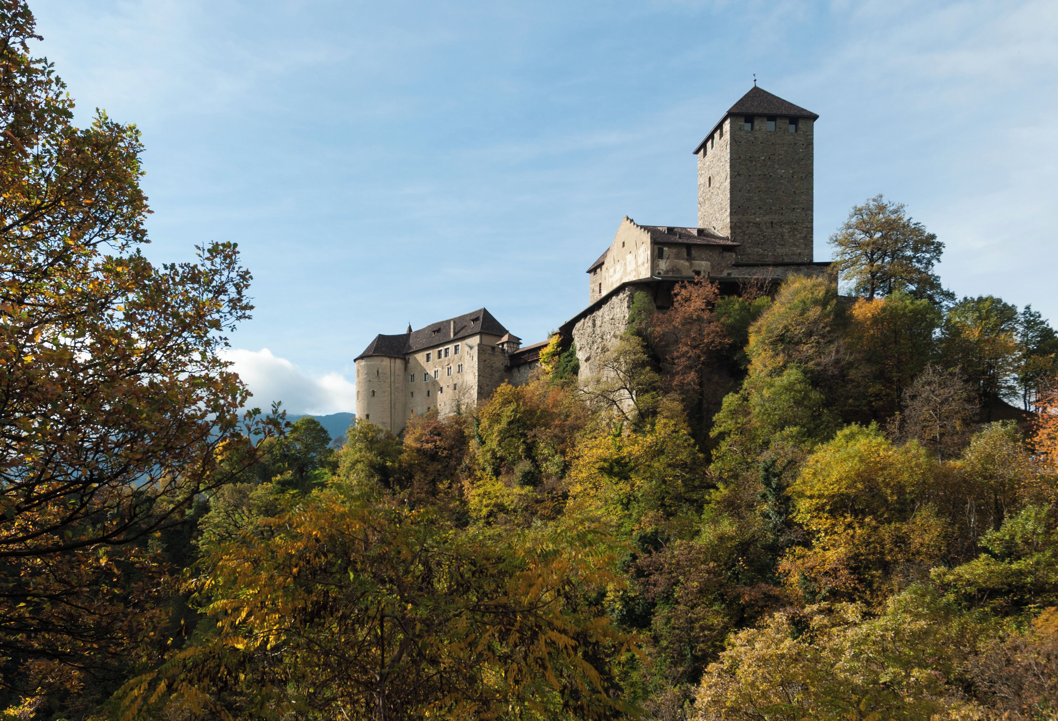 A historic castle on a hill surrounded by autumn foliage.