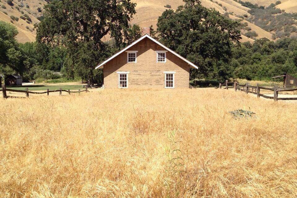 A wooden house surrounded by dry grassland and hills.