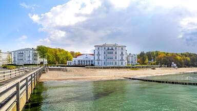 A coastal promenade with a wooden pier, white buildings, and a beach.