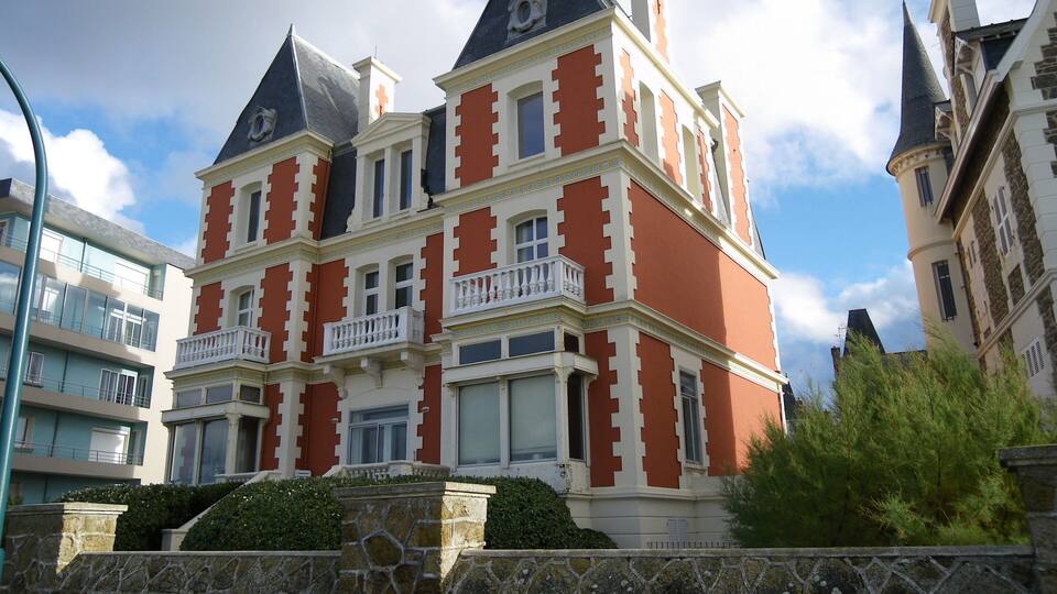 Un edificio de varios pisos con una fachada distintiva de color rojo y blanco, techos a dos aguas y balcones ornamentados.