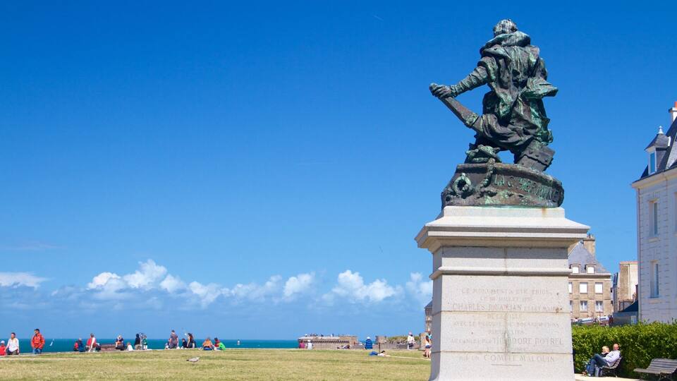 A statue of a man holding a sword on a pedestal, with a clear blue sky and a beach in the background.