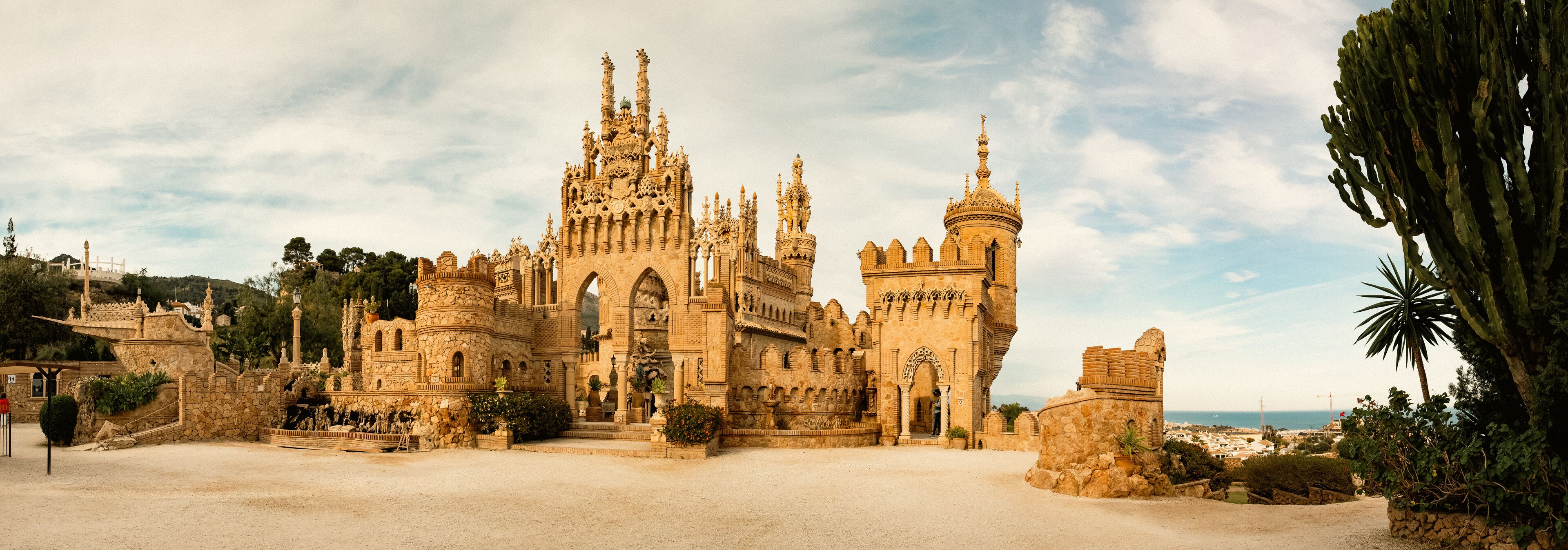 A historic castle with intricate architecture, a large courtyard, and a coastal backdrop.