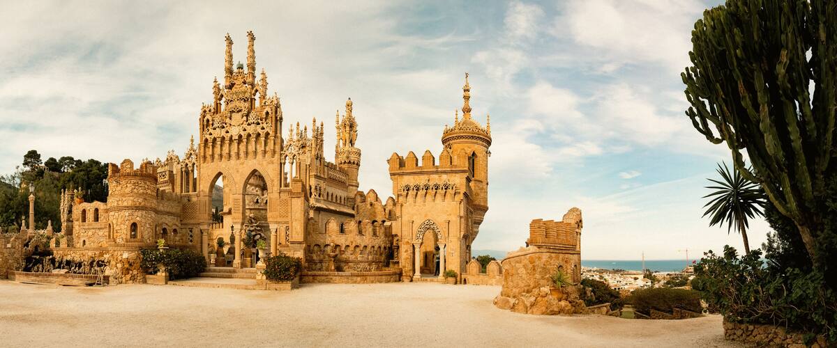 A historic castle with intricate architecture, a large courtyard, and a coastal backdrop.
