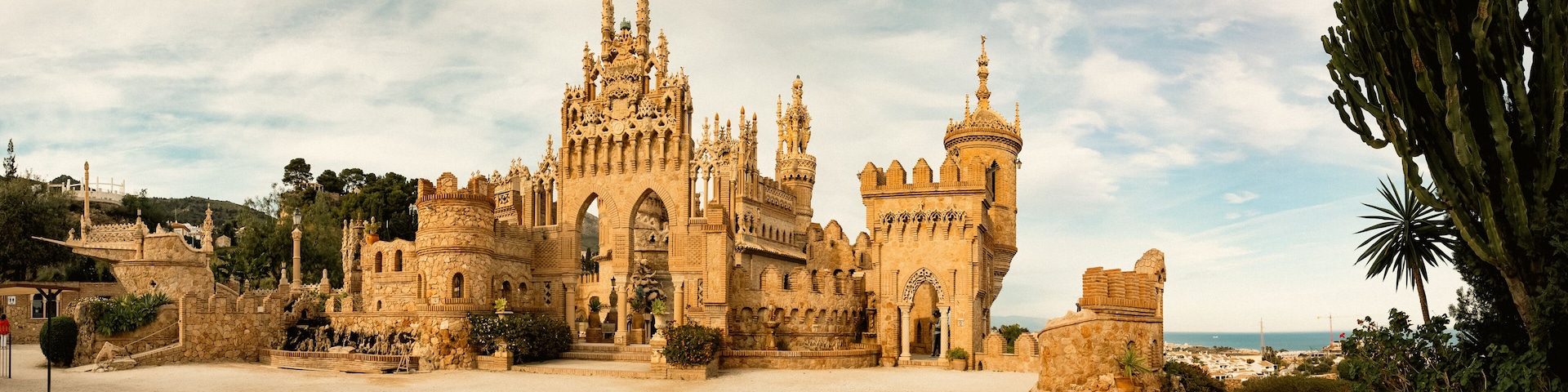 A historic castle with intricate architecture, a large courtyard, and a coastal backdrop.
