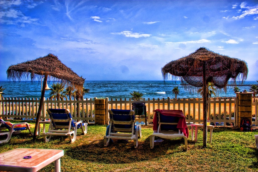 A beach with lounge chairs, thatched umbrellas, and a wooden fence overlooking the ocean.