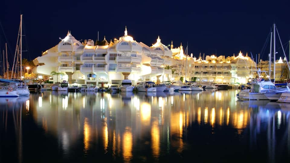 A marina at night with illuminated buildings and boats reflecting on the water.