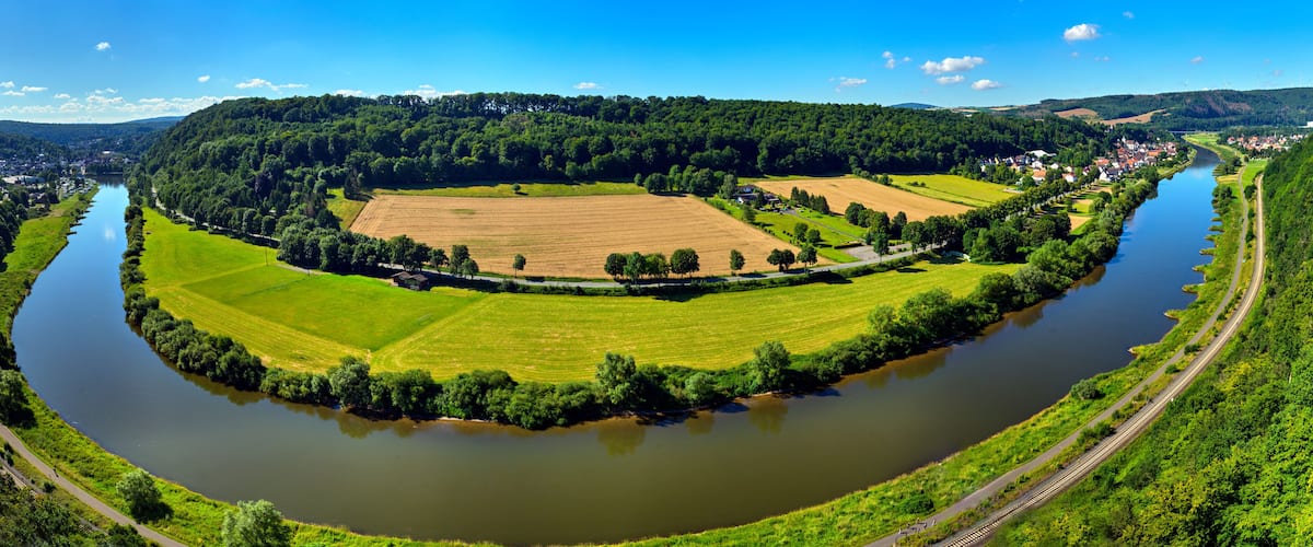A river winding through a lush valley with fields and a forested hill in the background.