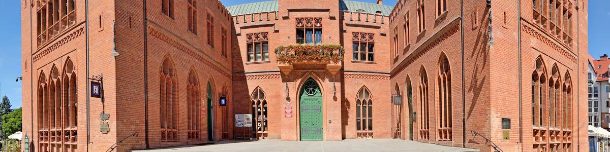 A large red brick building with a clock tower, arched windows, and a central entrance.