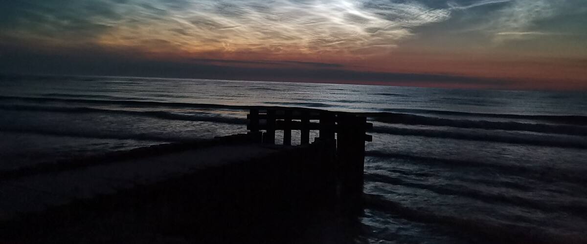 A bench overlooking a beach at sunset with a cloudy sky.