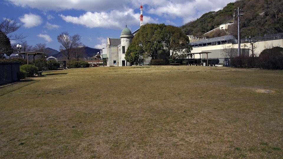 A large open grassy field with a building with a dome and a red tower in the background.