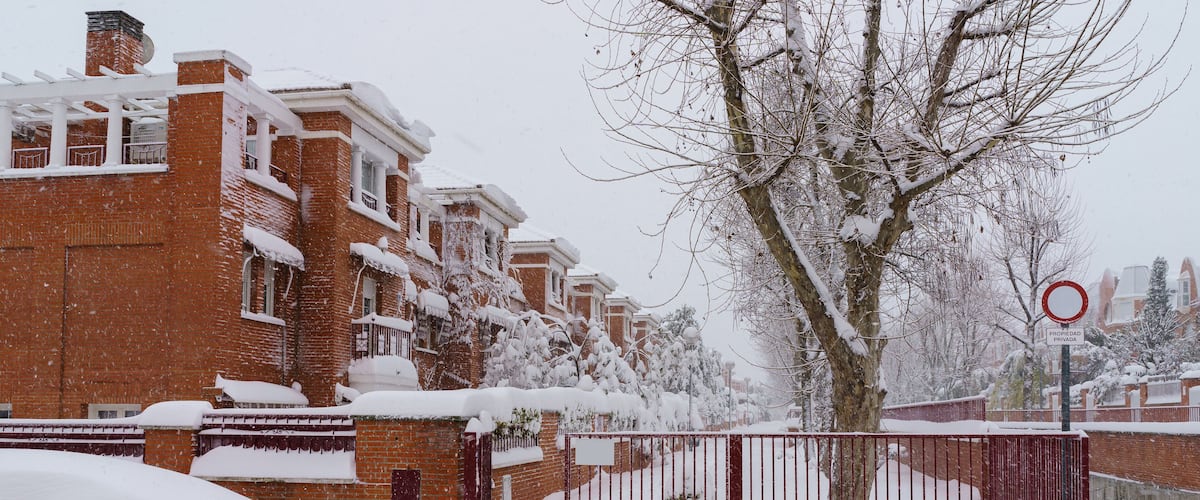 A snow-covered residential area with brick houses, a metal fence, and a 'propiedad privada' sign.