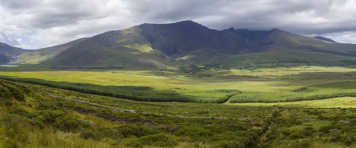 A mountainous landscape with a valley, green fields, and a stone wall.