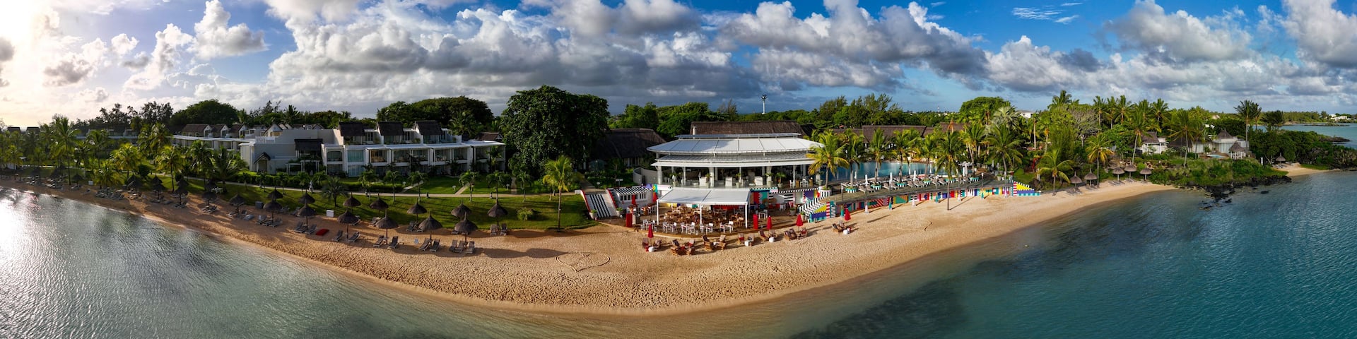 A tropical resort with a beach, palm trees, and a pool.