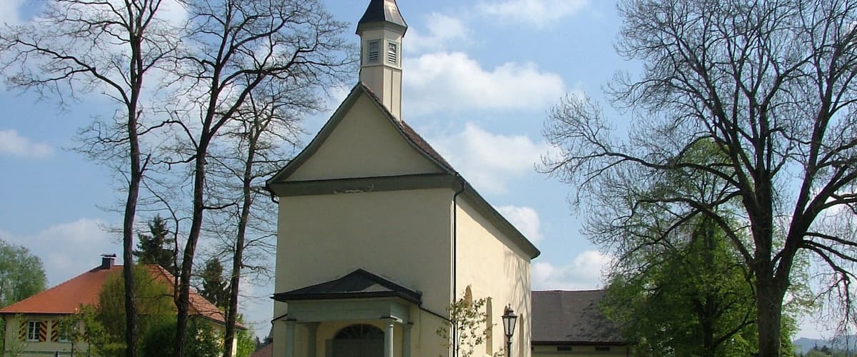 A small church with a steeple, surrounded by trees and a well-maintained lawn.