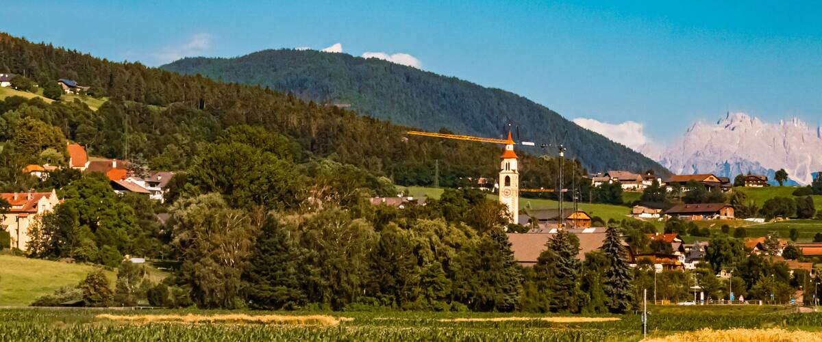 A rural landscape with a church tower, houses, and mountains in the background.