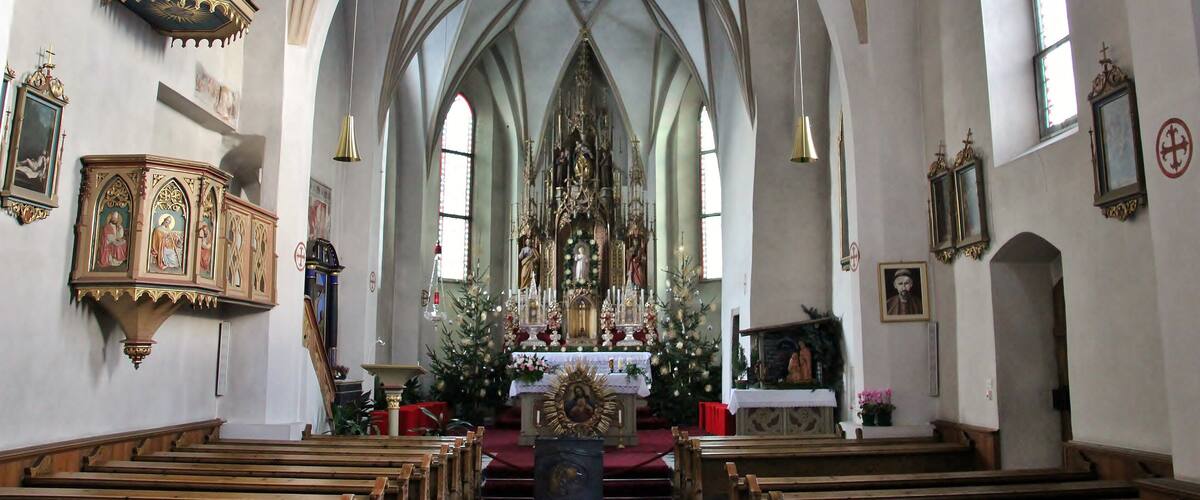 A church interior with high vaulted ceilings, wooden pews, and religious artwork.