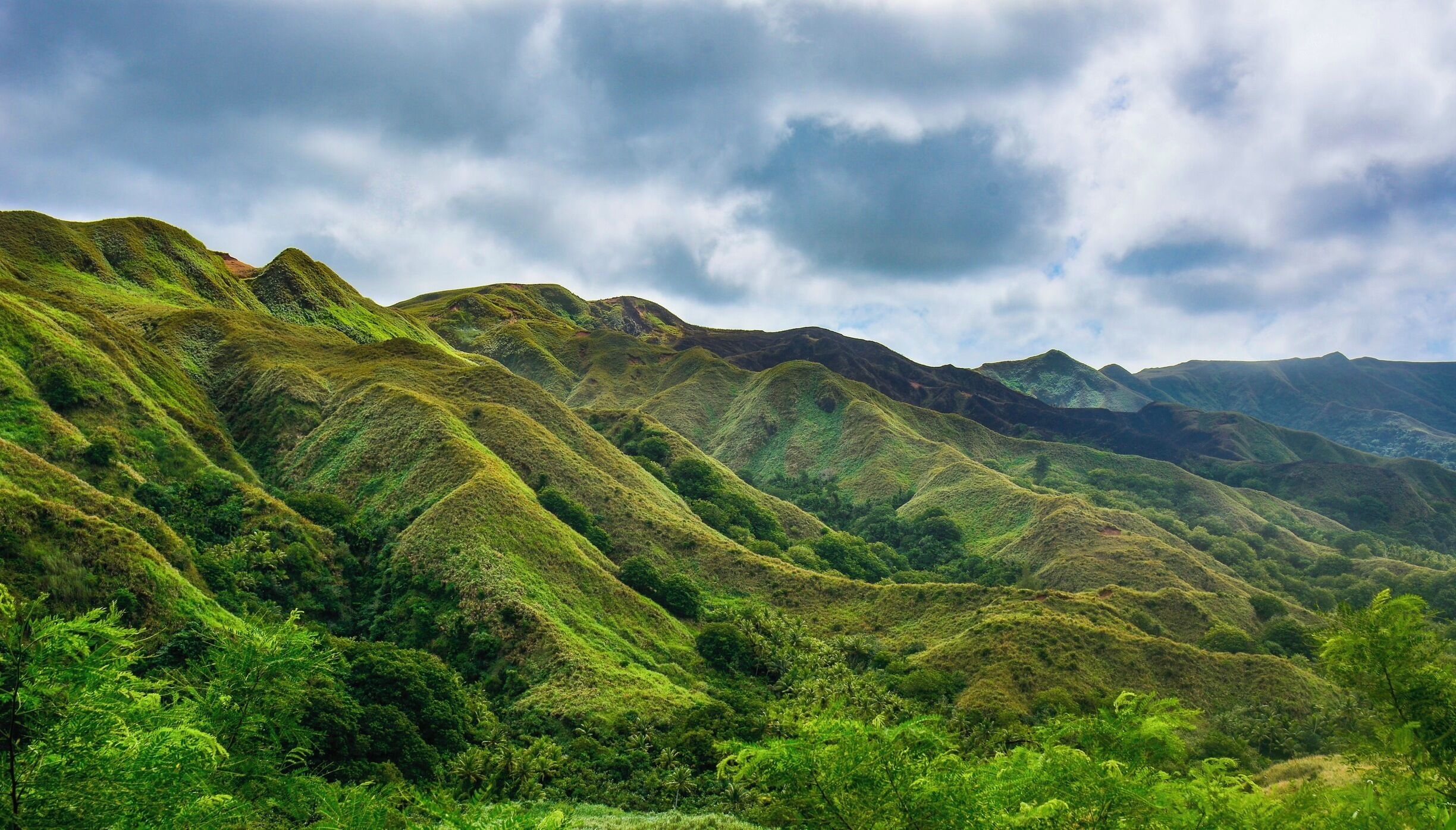 A lush green mountain range with dense vegetation and a cloudy sky.