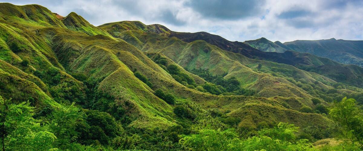 A lush green mountain range with dense vegetation and a cloudy sky.