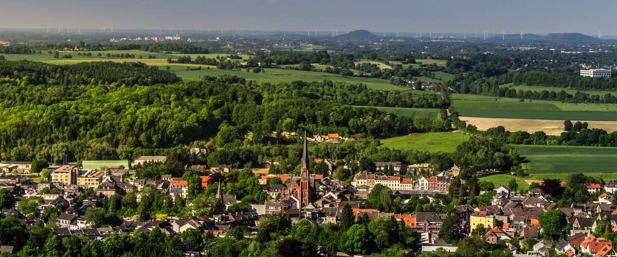 A town with a prominent church, surrounded by lush green fields and wind turbines in the distance.