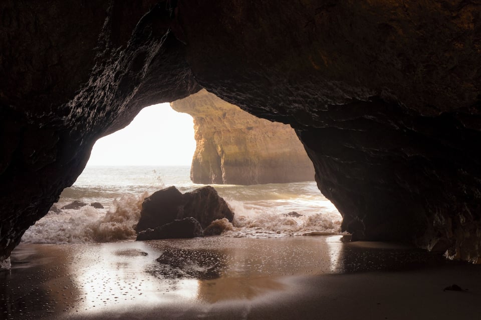 A cave opening to a beach with waves crashing onto the shore.
