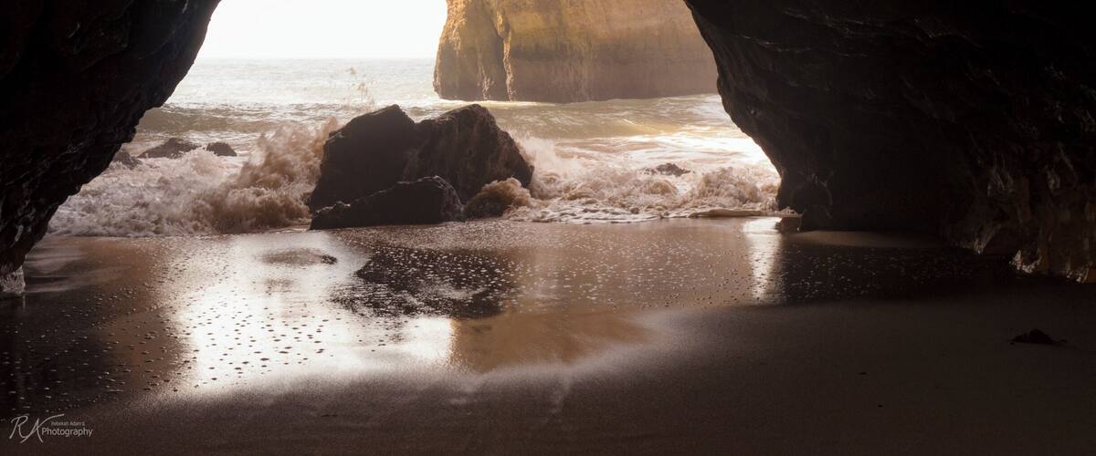 A cave opening to a beach with waves crashing onto the shore.