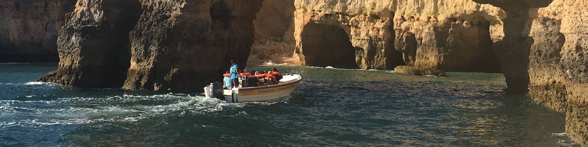 A boat navigating through a natural rock arch formation in a body of water.