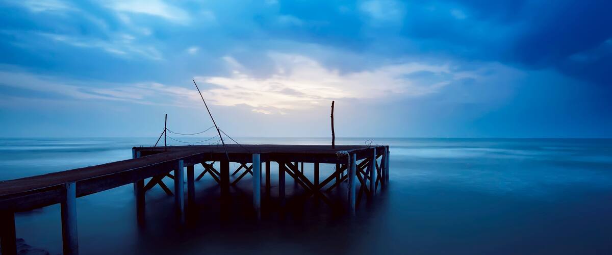 A wooden pier extending into calm waters under a cloudy sky.