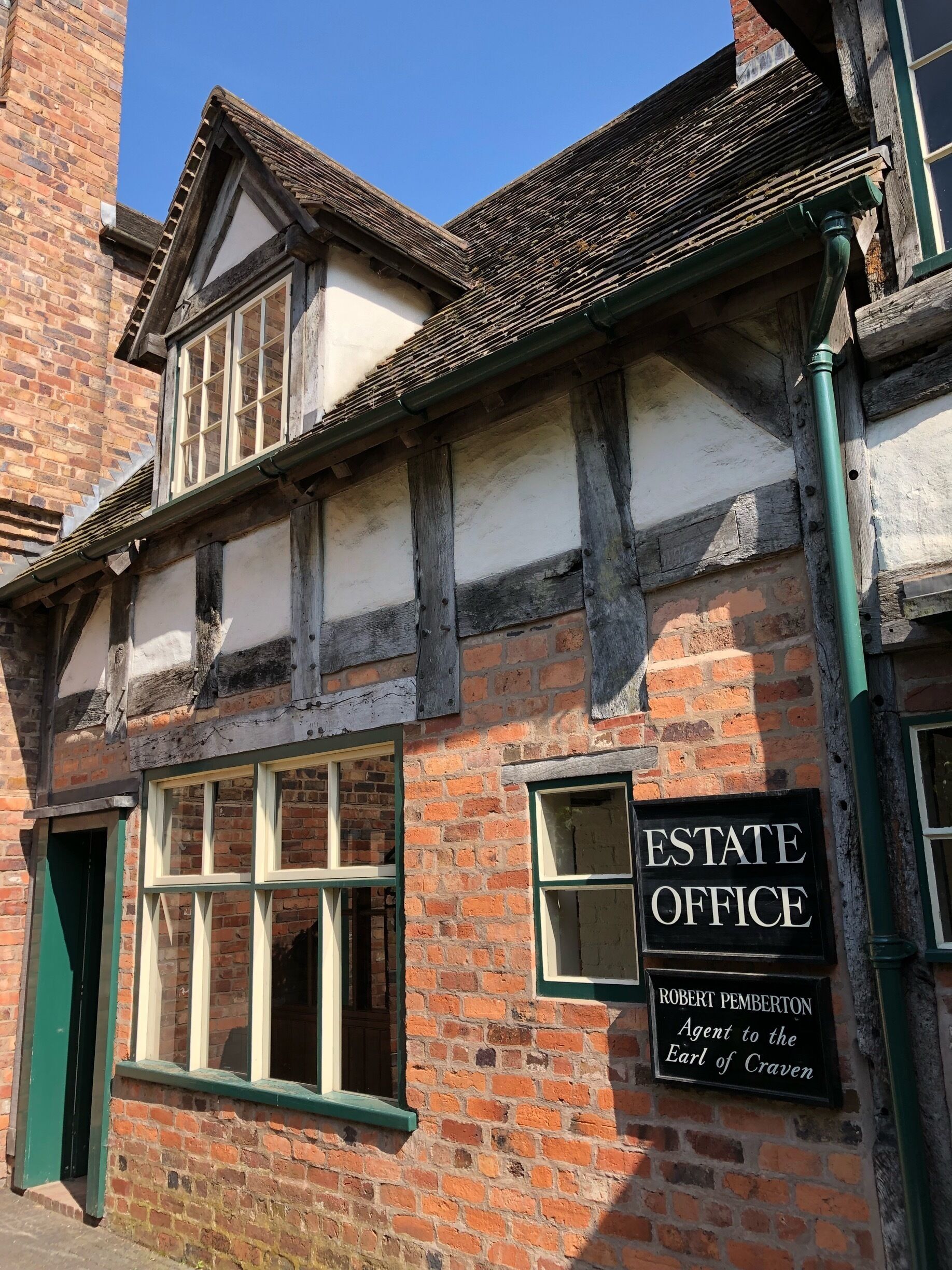 A traditional half-timbered building with a sign reading "ESTATE OFFICE" and "ROBERT PEMBERTON Agent to the Earl of Craven".