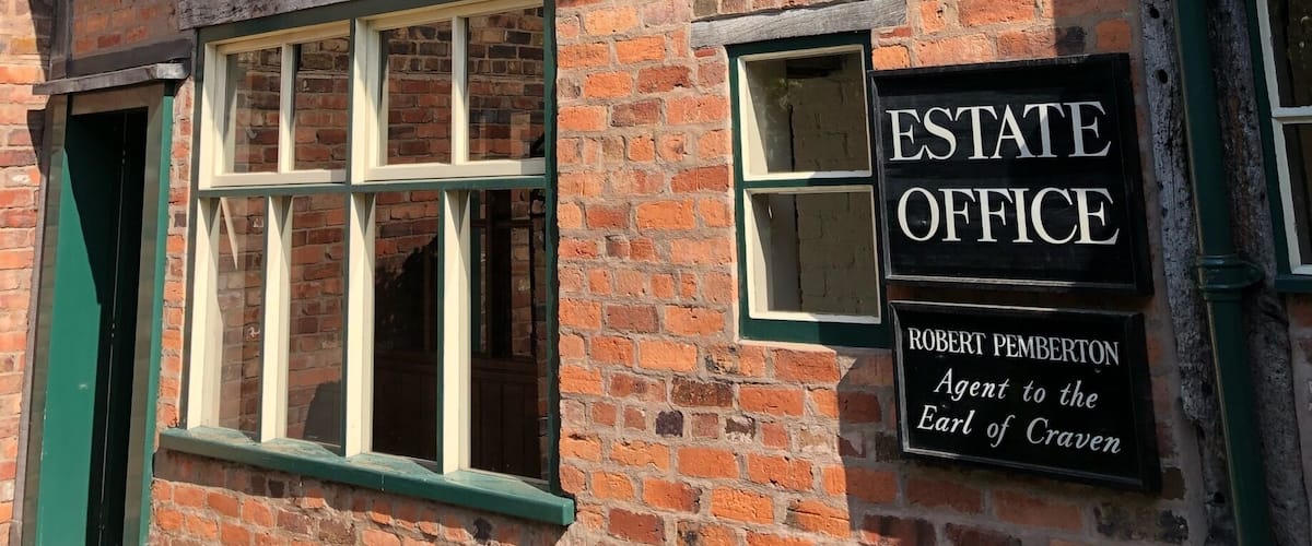 A traditional half-timbered building with a sign reading "ESTATE OFFICE" and "ROBERT PEMBERTON Agent to the Earl of Craven".