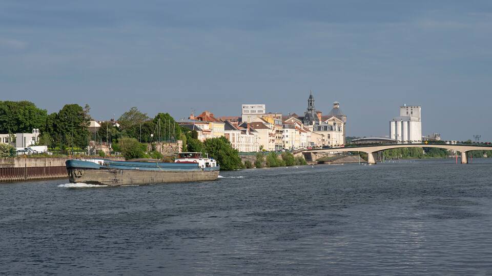 A river with a boat, a bridge, and historic buildings along the riverbank.