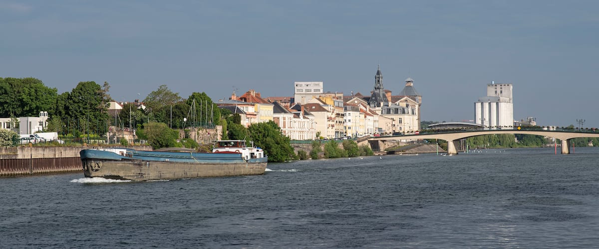 A river with a boat, a bridge, and historic buildings along the riverbank.
