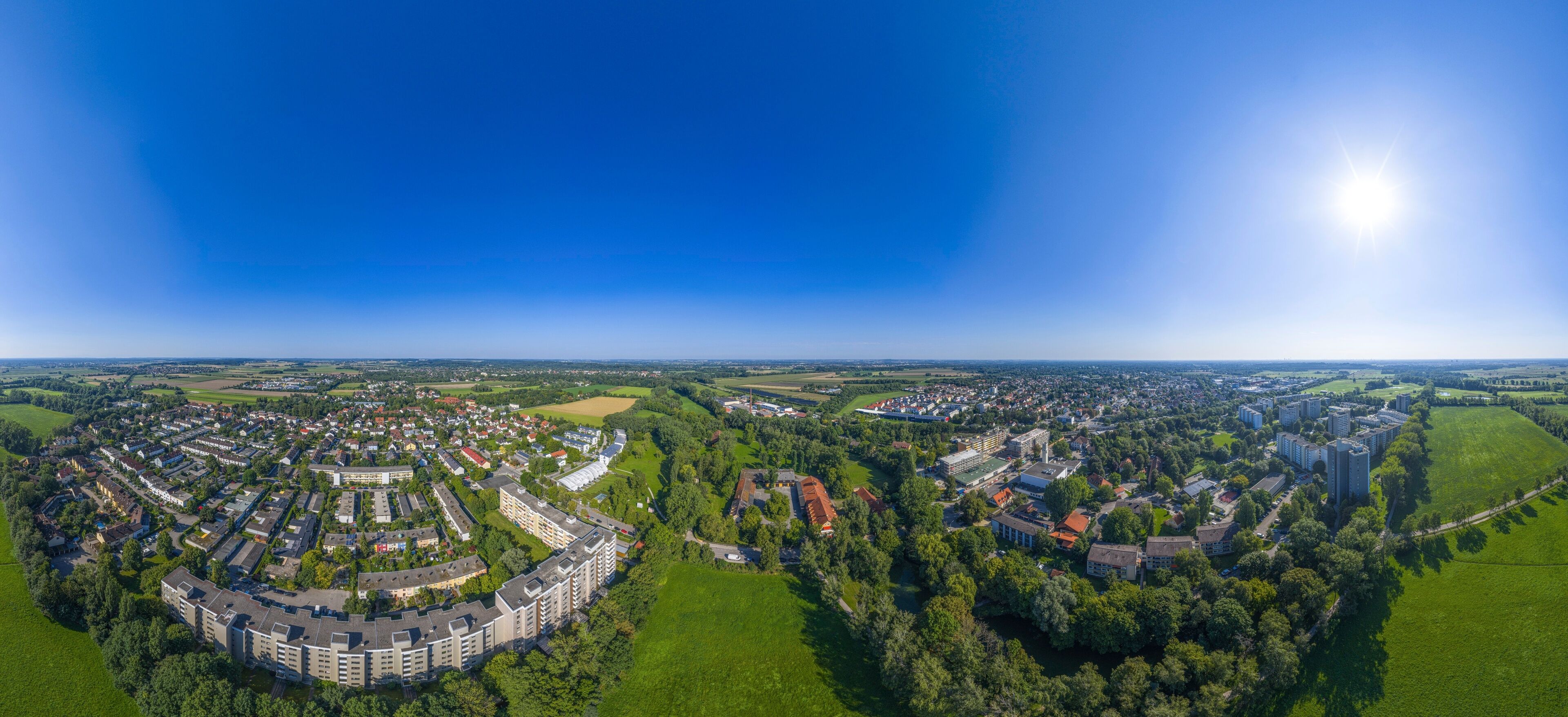 An aerial view of a town with residential areas, green fields, and a large building complex.