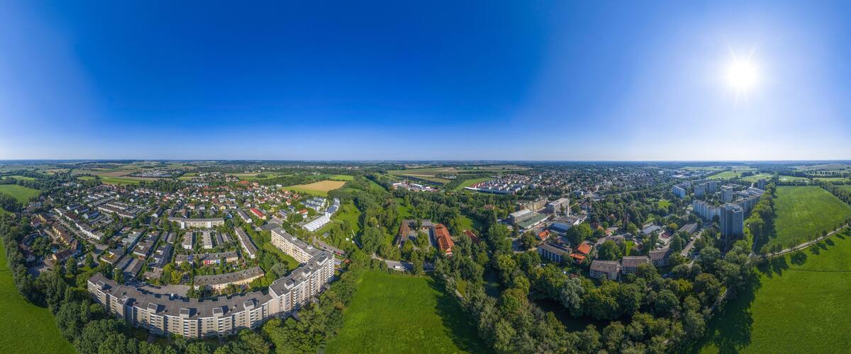 An aerial view of a town with residential areas, green fields, and a large building complex.