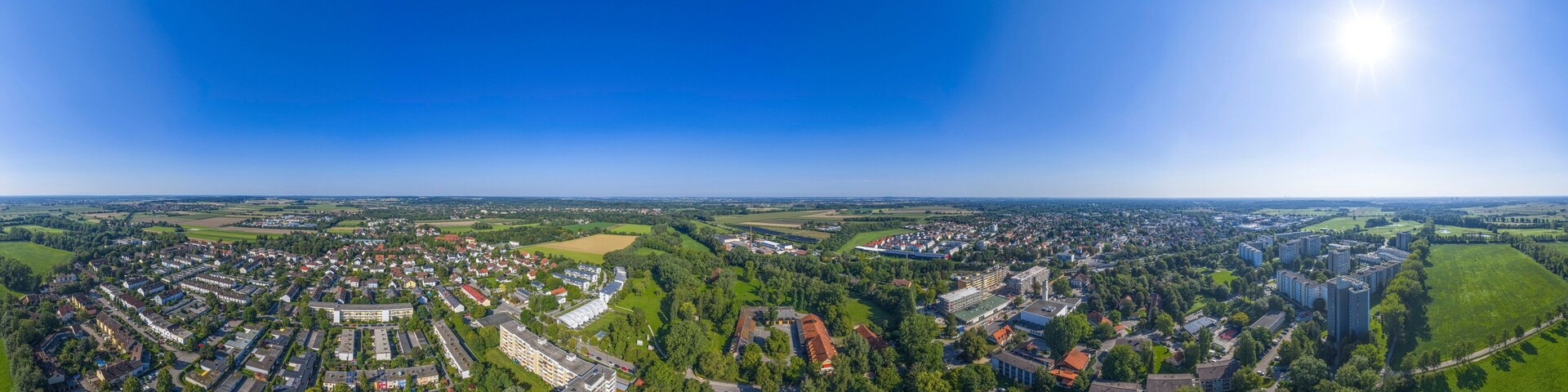 An aerial view of a town with residential areas, green fields, and a large building complex.