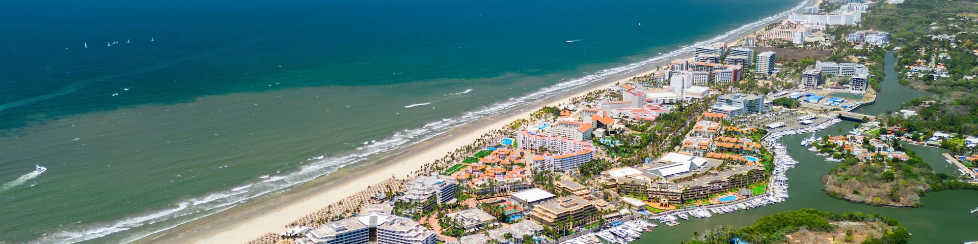 An aerial view of a coastal city with a beach, marina, and surrounding hills.