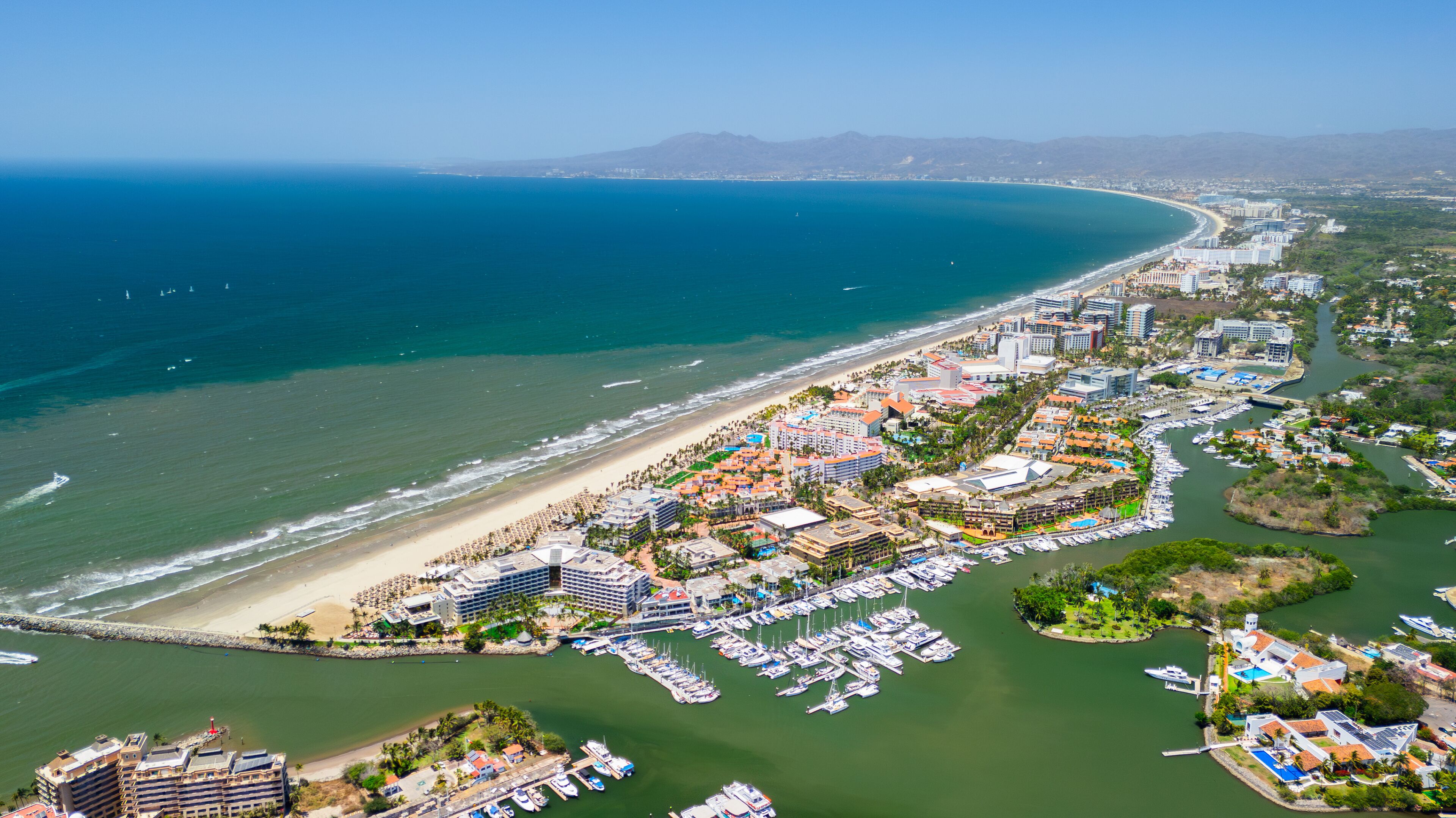 An aerial view of a coastal city with a beach, marina, and surrounding hills.