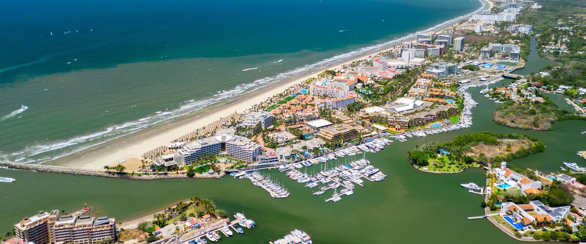An aerial view of a coastal city with a beach, marina, and surrounding hills.