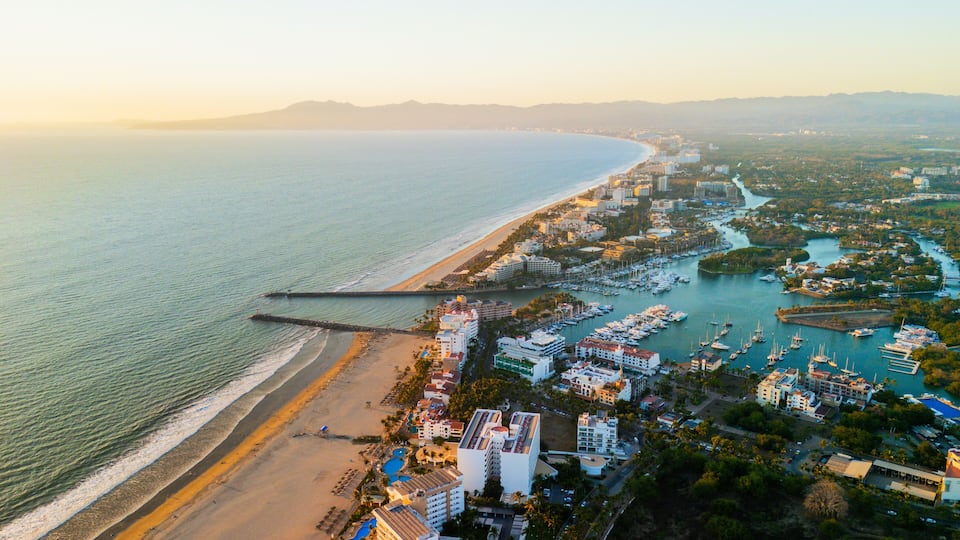 A coastal cityscape with a beach, marina, and urban buildings.