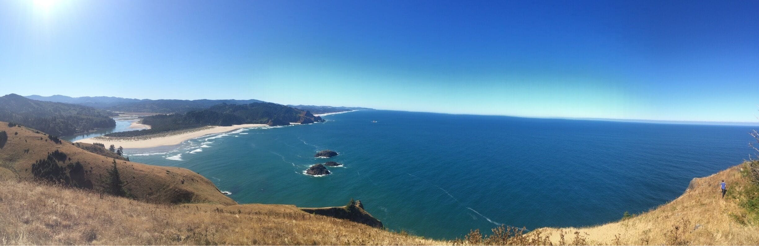 Paisagem costeira com vista ampla do oceano, praia de areia e relevo acidentado.