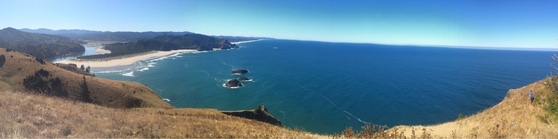 A coastal landscape with a clear view of the ocean, sandy beach, and a hilly terrain.