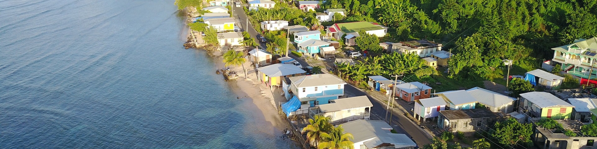 Un pueblo costero con casas a lo largo de la orilla, una playa y una colina boscosa al fondo.