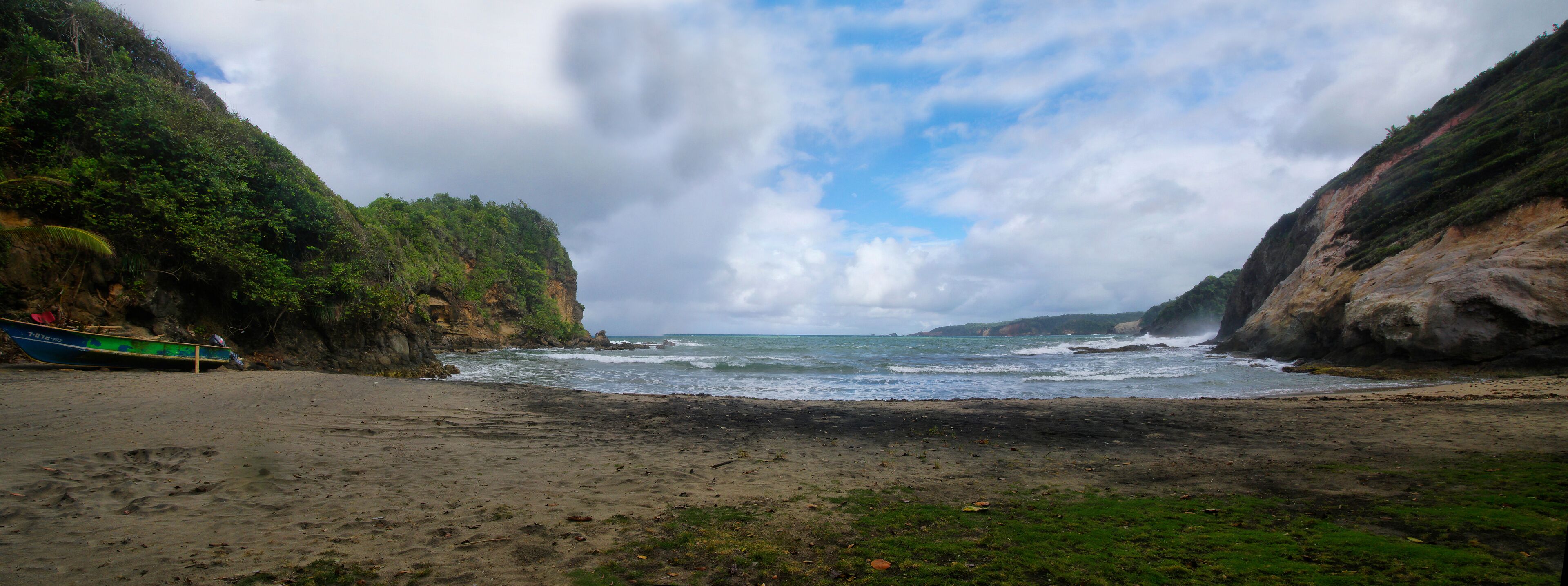 A beach with a boat on the left and rocky cliffs on both sides.