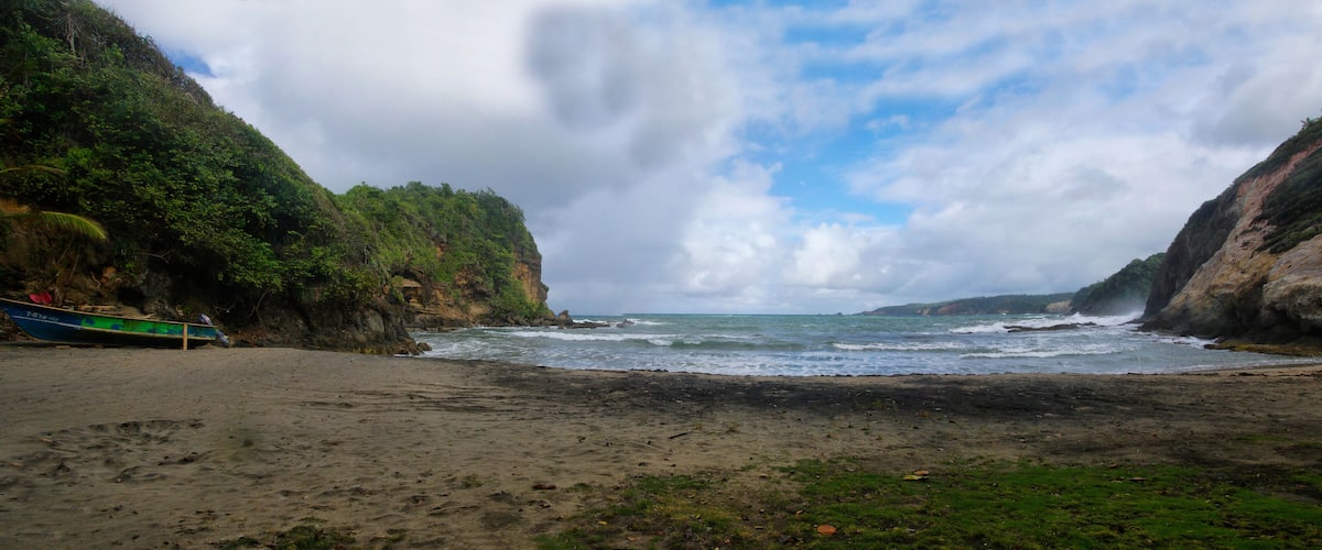 A beach with a boat on the left and rocky cliffs on both sides.