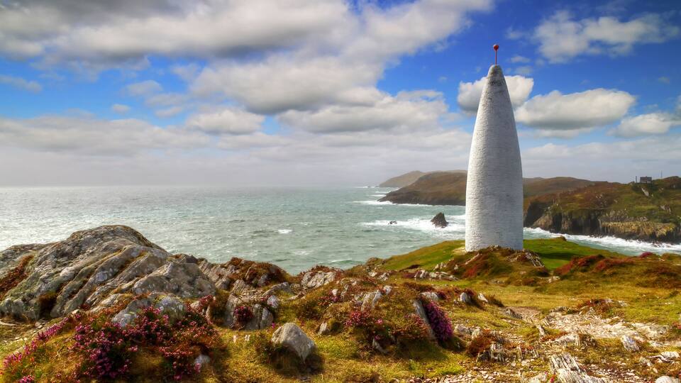 A coastal landscape with a prominent lighthouse, rocky terrain, and the ocean.