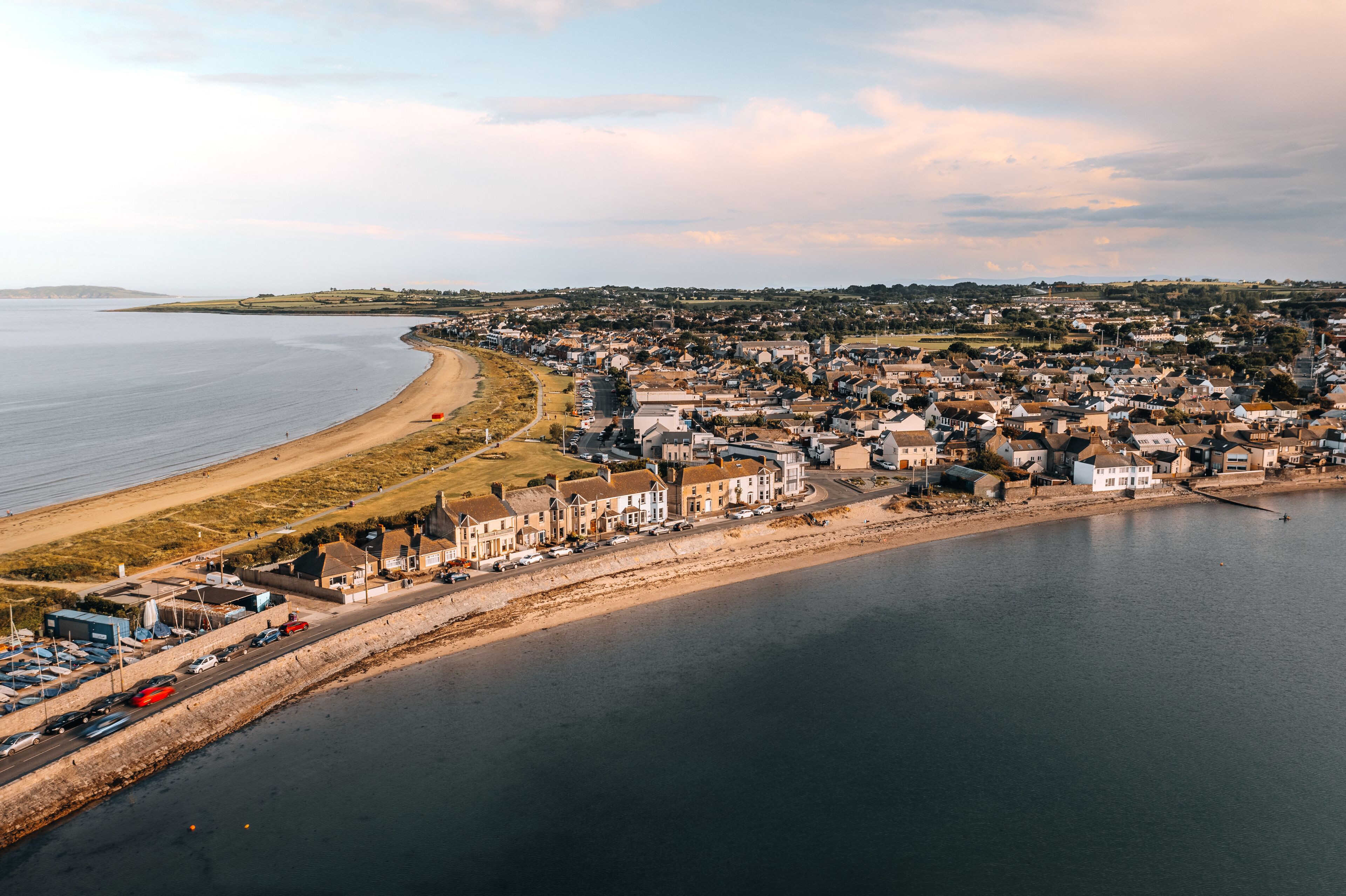 Aerial photograph of the charming beachfront town of Skerries, Ireland, captured around sunset. The image showcases the expansive beach, residential homes, and surrounding countryside.