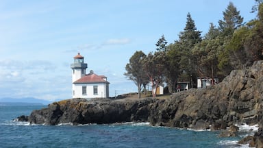 A lighthouse on a rocky coastline with clear blue waters and trees.